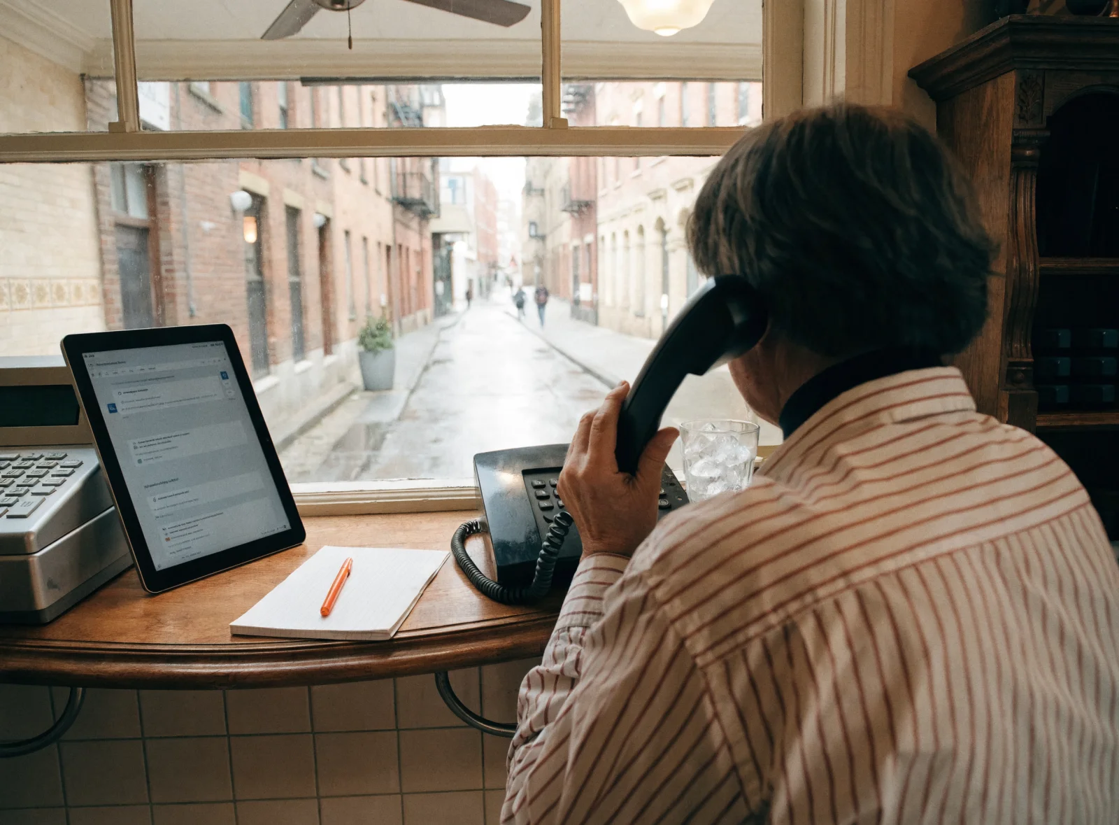 Hands answering a desk phone at a shop counter beside a tablet